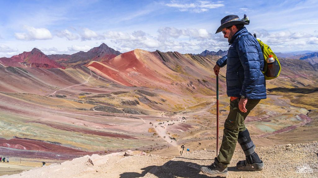 Man walking on the Rainbow Mountain (Vinicunca) in Cusco, with colorful mountains in the background, avoiding altitude sickness and enjoying the breathtaking view.