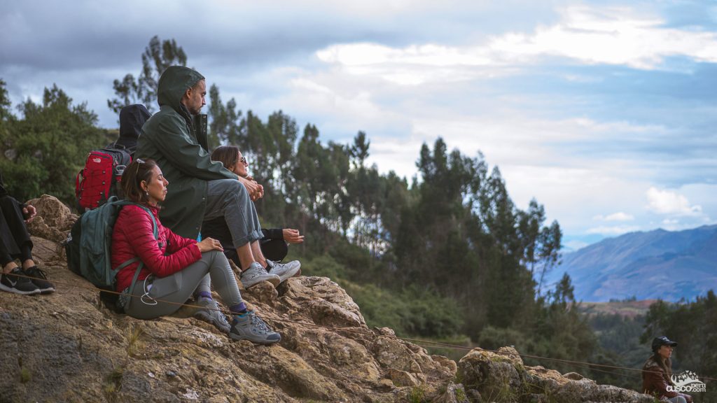 Tourists resting on the slope of a mountain in Cusco, with forest and mountains in the background, avoiding altitude sickness.